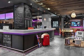 Un espace bar moderne doté d’un comptoir d’enregistrement, de sièges et d’un écran numérique.