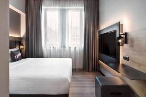 A hotel room with a bed, a TV, a bedside table, and a window with curtains. - Moxy Bucharest Old Town (Bucharest)
