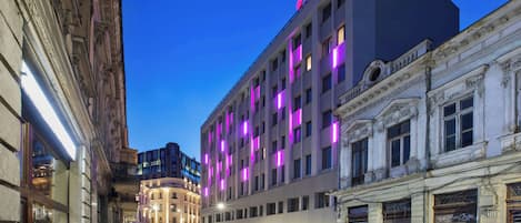 A multi-story hotel with a modern facade, illuminated windows, and a prominent neon sign on the top.