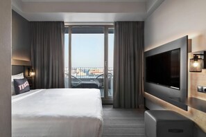 Camera d'albergo con un letto grande, una televisione a schermo piatto, una scrivania e un balcone con vista sulla città.