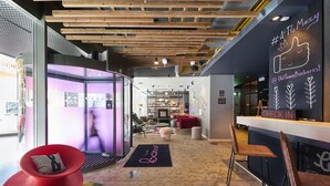 A modern interior with a wooden ceiling, a reception desk, and a seating area with a red chair and a brown chair. - Moxy Bucharest Old Town (Bucharest)