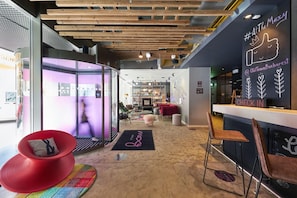 A modern interior with a reception desk, seating area, and a glass partition. - Moxy Bucharest Old Town (Bucharest)
