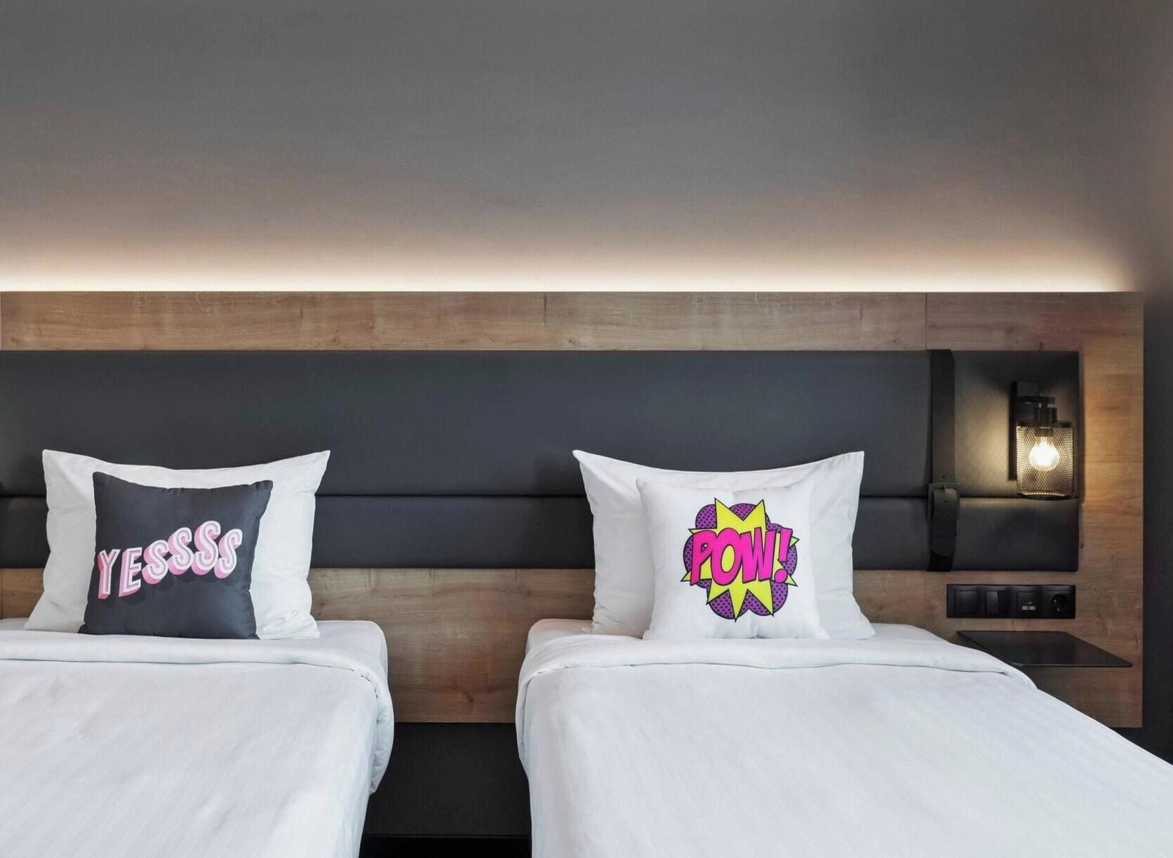 A hotel room with two beds, each with a pillow featuring a pop art design.