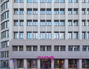 Un hotel a più piani con una facciata moderna, caratterizzato da una segnaletica con contorno in neon rosa.
