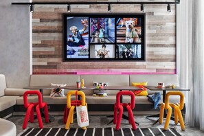 Un salon moderne avec un canapé, une table basse et des fauteuils colorés. Un téléviseur est fixé au mur, au-dessus de l’espace détente.