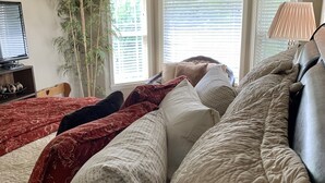 A neatly made bed with multiple pillows and a red blanket, a television on a shelf, and a large window with blinds. - 2 king 2 twin beds 3Bed 2.5 Ba cozy Mer Home near Village with Hot tub (Meridian)