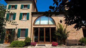 Un bâtiment à deux étages, construit en briques, avec des volets verts, une grande porte d’entrée en verre en arc de cercle et un banc devant.
