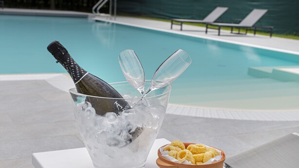Une scène de bord de piscine avec une bouteille de champagne, de la glace et des verres dans un seau, ainsi qu'un bol de chips.