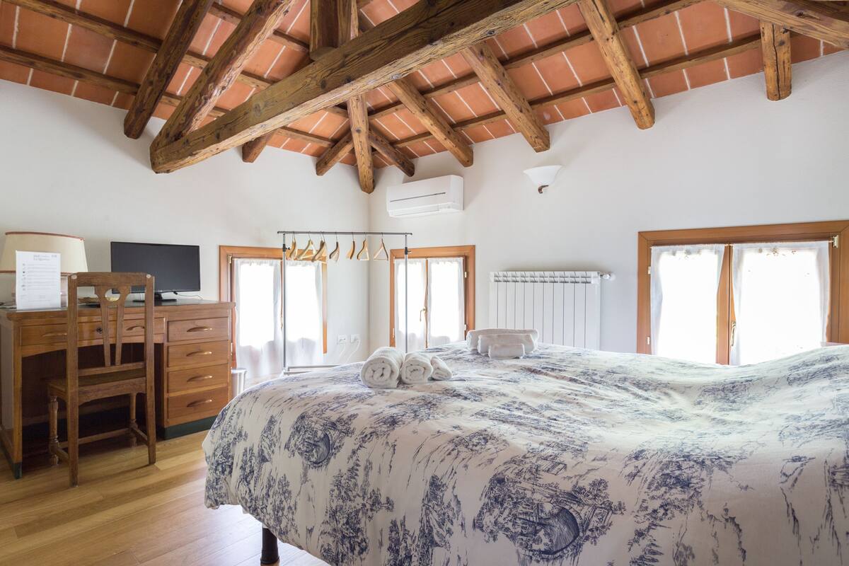 Ein Schlafzimmer mit einem Holztisch, einem Bett mit gemustertem Überwurf und einer rustikalen Decke.
