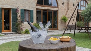 Une table avec un grand seau à glace, une bouteille et un bol de chips, placée à l’extérieur d’un bâtiment en briques doté de grandes fenêtres et d’une échelle en bois.
