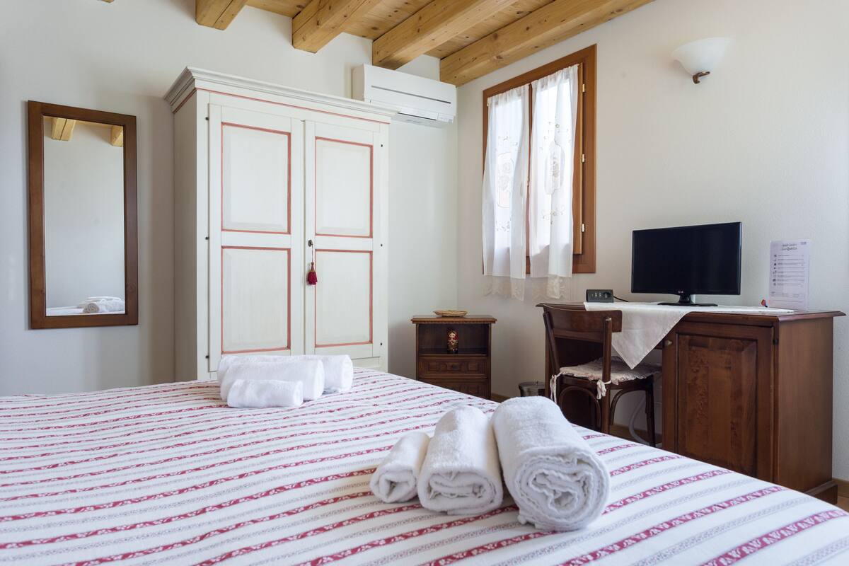 Ein Hotelzimmer mit Bett, Kleiderschrank, Schreibtisch, Fernseher und einem Fenster mit Vorhängen.