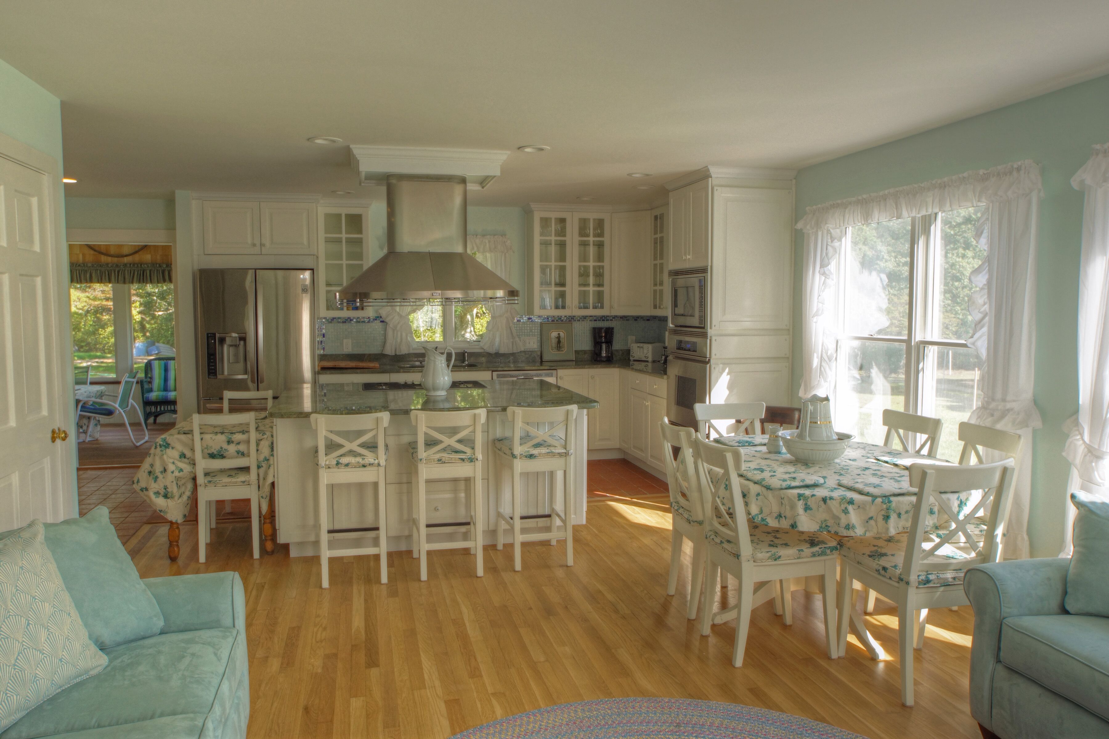 A spacious kitchen with white cabinetry, a central island, and a dining area with white chairs.