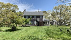 Une maison à deux étages avec un grand jardin devant, une terrasse en bois et un garage.