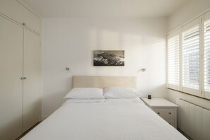 A bedroom with a bed, a nightstand, a wardrobe, and a window with blinds.
