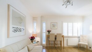 Een woonkamer met een bank, een eettafel met stoelen, een radiator en een kroonluchter.