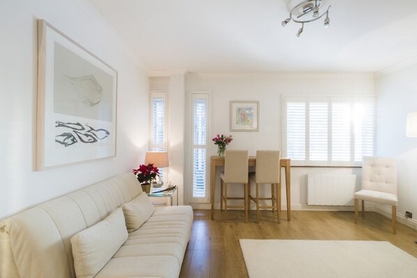 A living room with a sofa, a dining table with chairs, a radiator, and a chandelier.