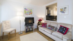 Een woonkamer met een bank, een fauteuil, een televisie, een vloerlamp en kunst aan de muren.