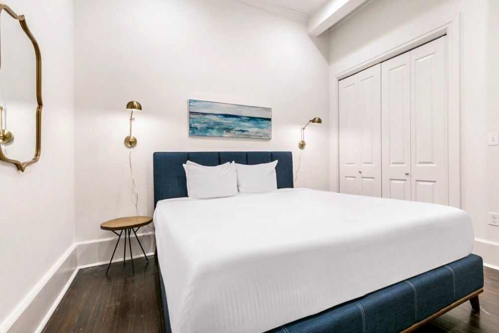 Un dormitorio con una cama grande, dos lámparas de noche, una mesita y un cuadro en la pared.