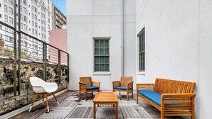 A rooftop terrace with wooden furniture, a stone wall, and a view of a cityscape.