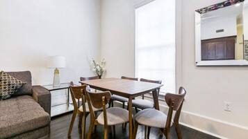 Un comedor con una mesa de madera y seis sillas, un sofá, una lámpara y un florero con ramas.