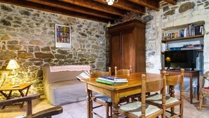 A cozy room with a stone wall, wooden furniture, a television, and bookshelves. - Gîte du Pigeonnier, 3 Épis, Mas Médaille (arles)