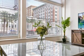 Enjoy a city view from the large window in this stylish room, featuring a glass table, a potted plant, and a wooden cabinet.