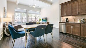 A modern kitchen with dark wood cabinets, a stainless steel dishwasher, and a dining area with a table and blue chairs. - Stunning Canal St Views • Steps to Bourbon (New Orleans)