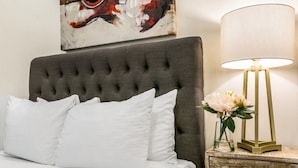 Ein Bett mit einem geblatteten Kopfteil, weißen Kissen und einem Nachttisch mit Lampe und Blumenvase.