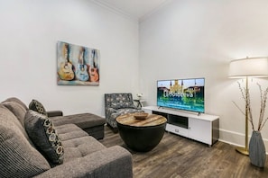 Un salon moderne avec un canapé gris, un fauteuil à motifs, une table basse noire, un téléviseur à écran plat et un tableau représentant des guitares.