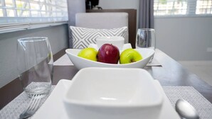 Una mesa de comedor con un plato blanco, un bol de fruta y un vaso de agua.