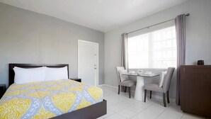 Una habitación de hotel con una cama, una mesa de comedor con sillas, una ventana con cortinas y un armario.