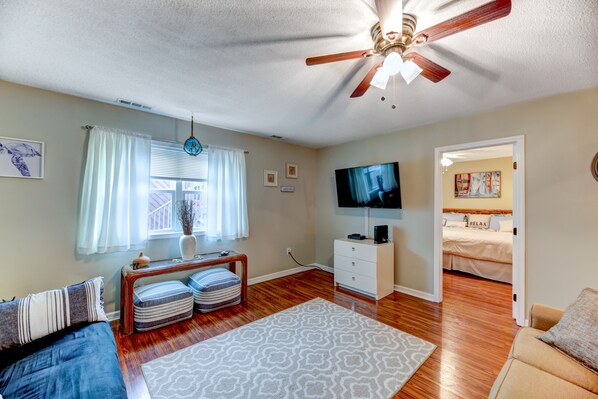 A spacious living room with a ceiling fan, a flat-screen TV, a sofa, a coffee table, and a patterned rug.