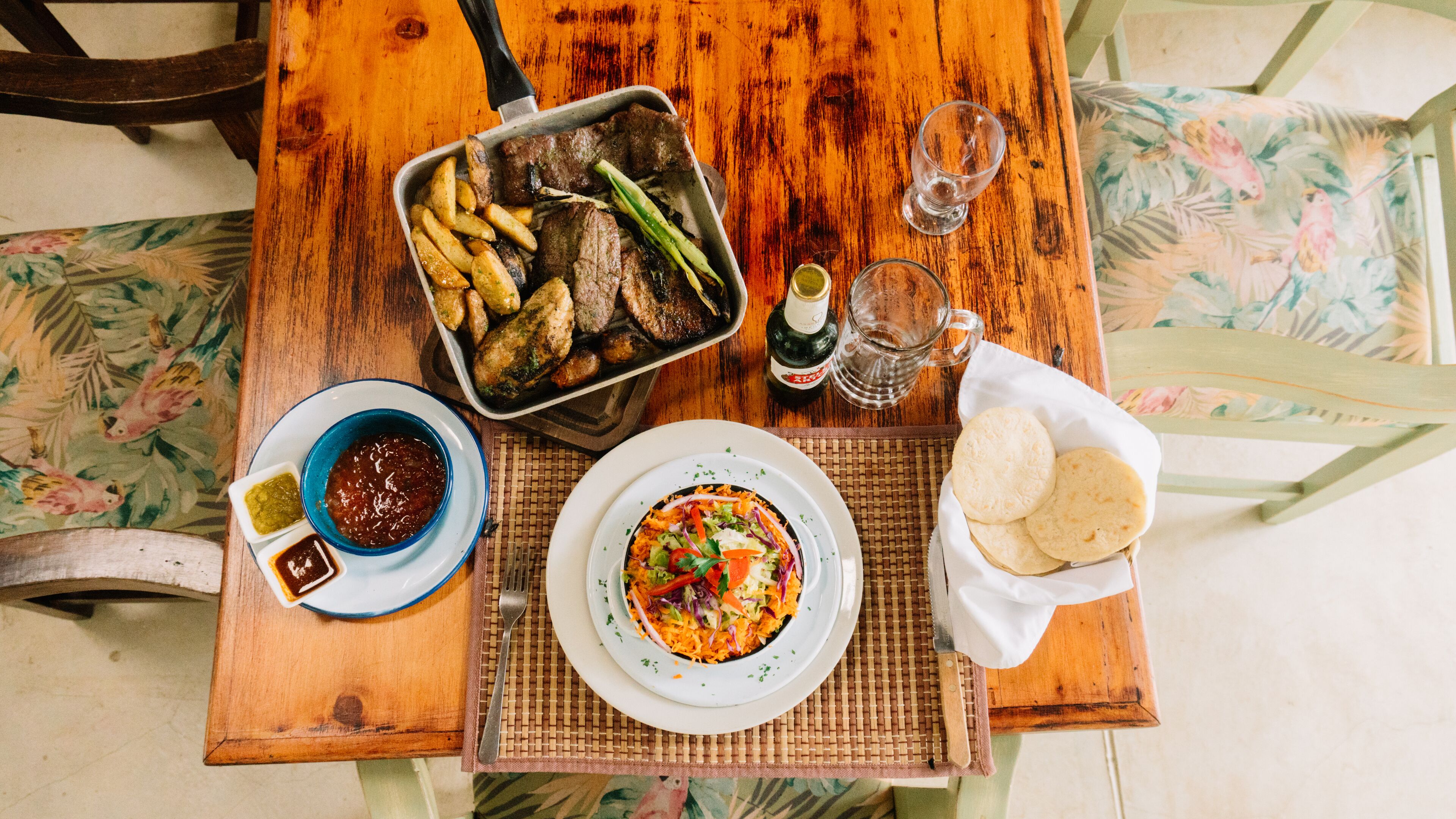 A wooden table with a meal consisting of a plate of rice with vegetables, a bowl of sauce, a plate of fried potatoes, and a basket of flatbreads.