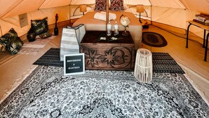 Interior acogedor de una carpa con una cama, almohadas, un globo terráqueo y un cartel de bienvenida.