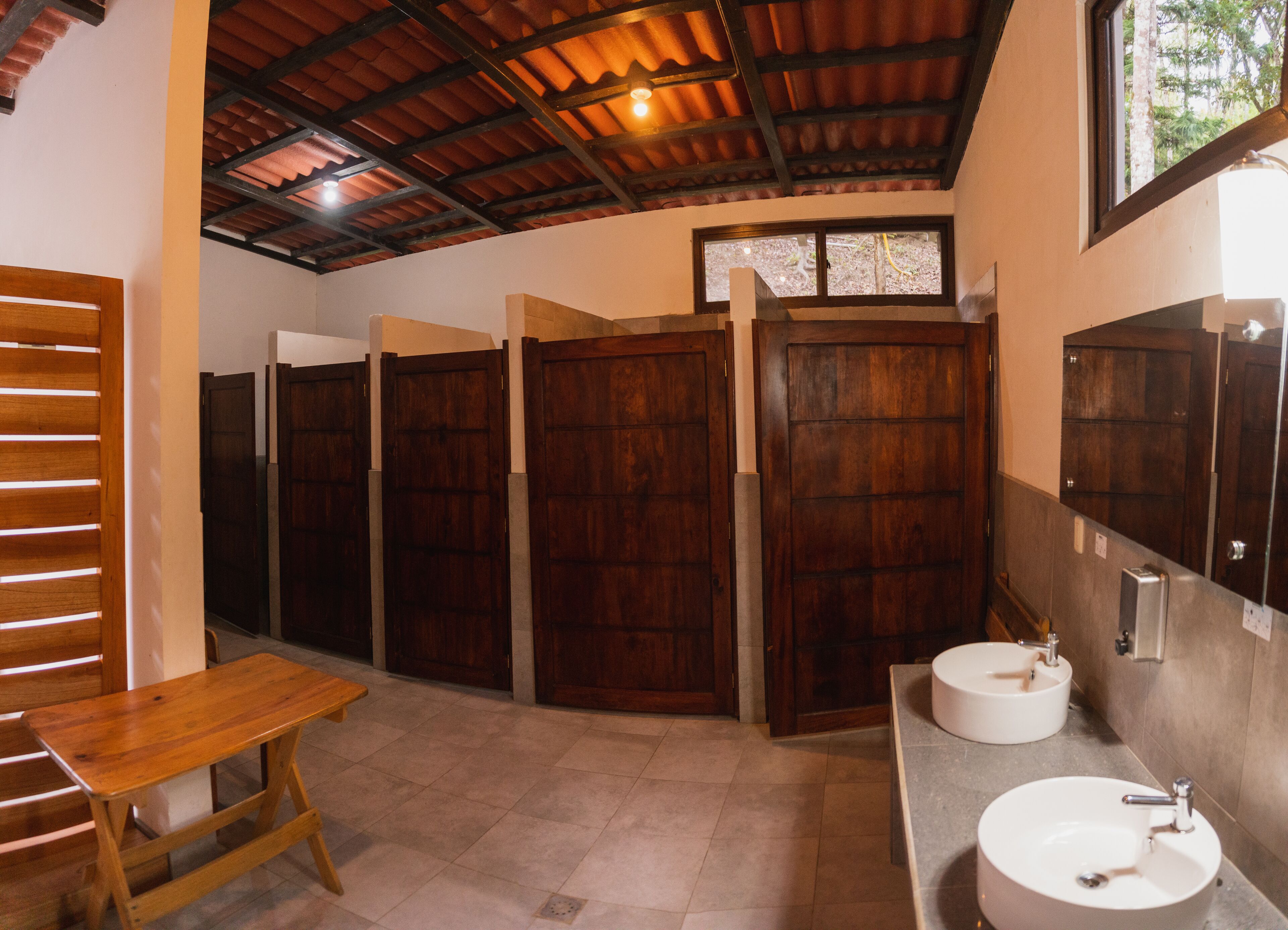 Un baño con cabinas de madera, un banco de madera y dos lavamanos.