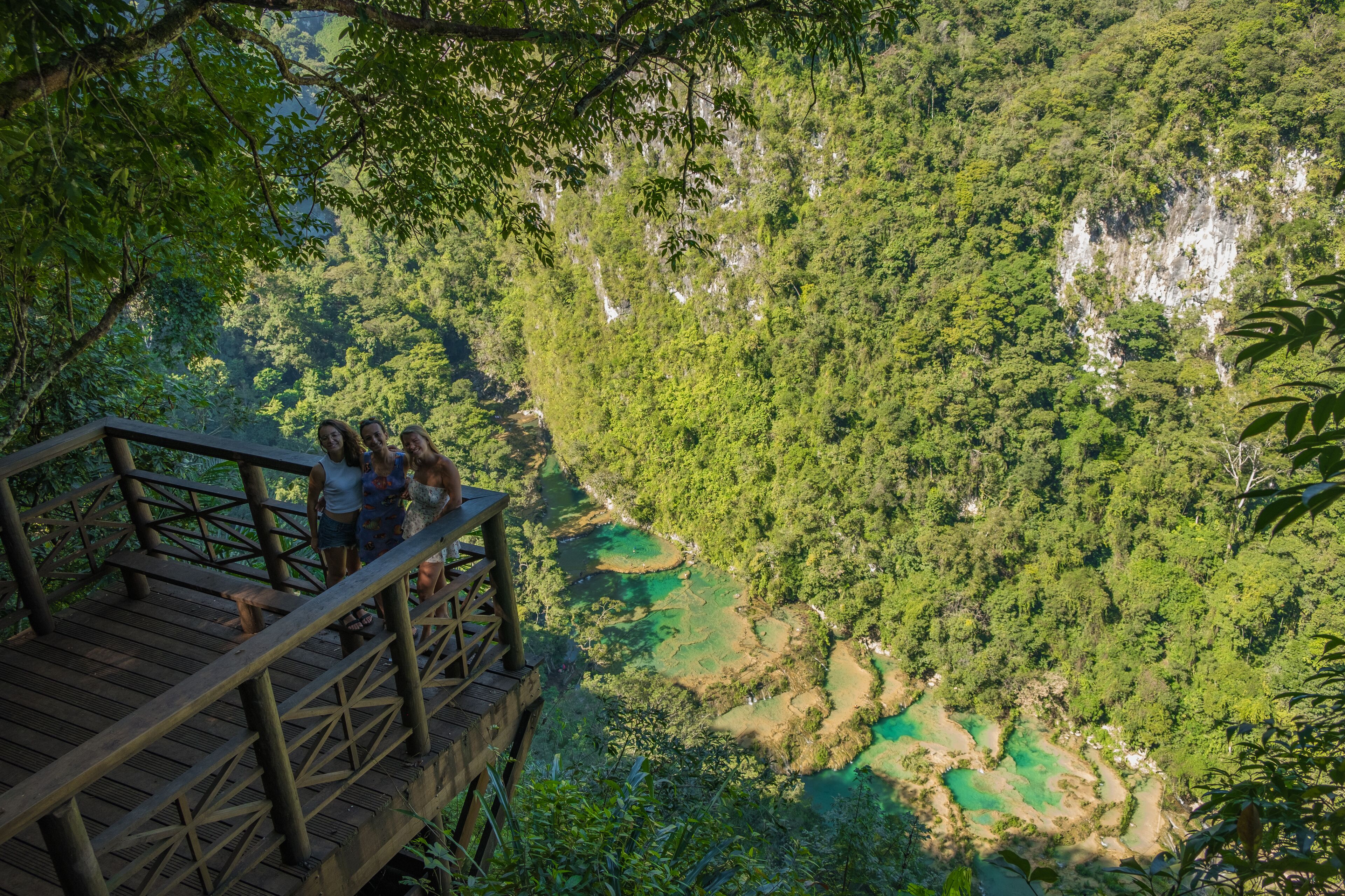 A wooden observation deck with a railing overlooking a lush green valley with clear water bodies.
