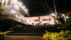 Un edificio de varios pisos con una escalera que conduce a la entrada, rodeado de vegetación.