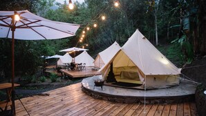 Un campamento con varias tiendas de campaña, una terraza de madera y luces colgantes.