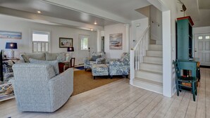 Un salón amplio con un sofá grande, dos sillones, una mesa de centro y una escalera que lleva a otro nivel.