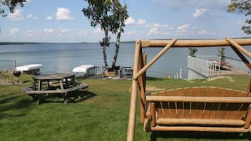 Relax by the serene lake with a swing and picnic table in a peaceful, fenced area surrounded by trees and shrubs.