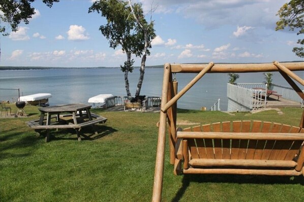 Relax by the serene lake with a swing and picnic table in a peaceful, fenced area surrounded by trees and shrubs.