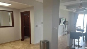 Una stanza spaziosa con pavimento in legno, un cestino, una porta e un angolo salotto con tavolo e sedie.