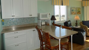Cozinha com armários brancos, micro-ondas e sala de jantar com mesa e cadeiras.