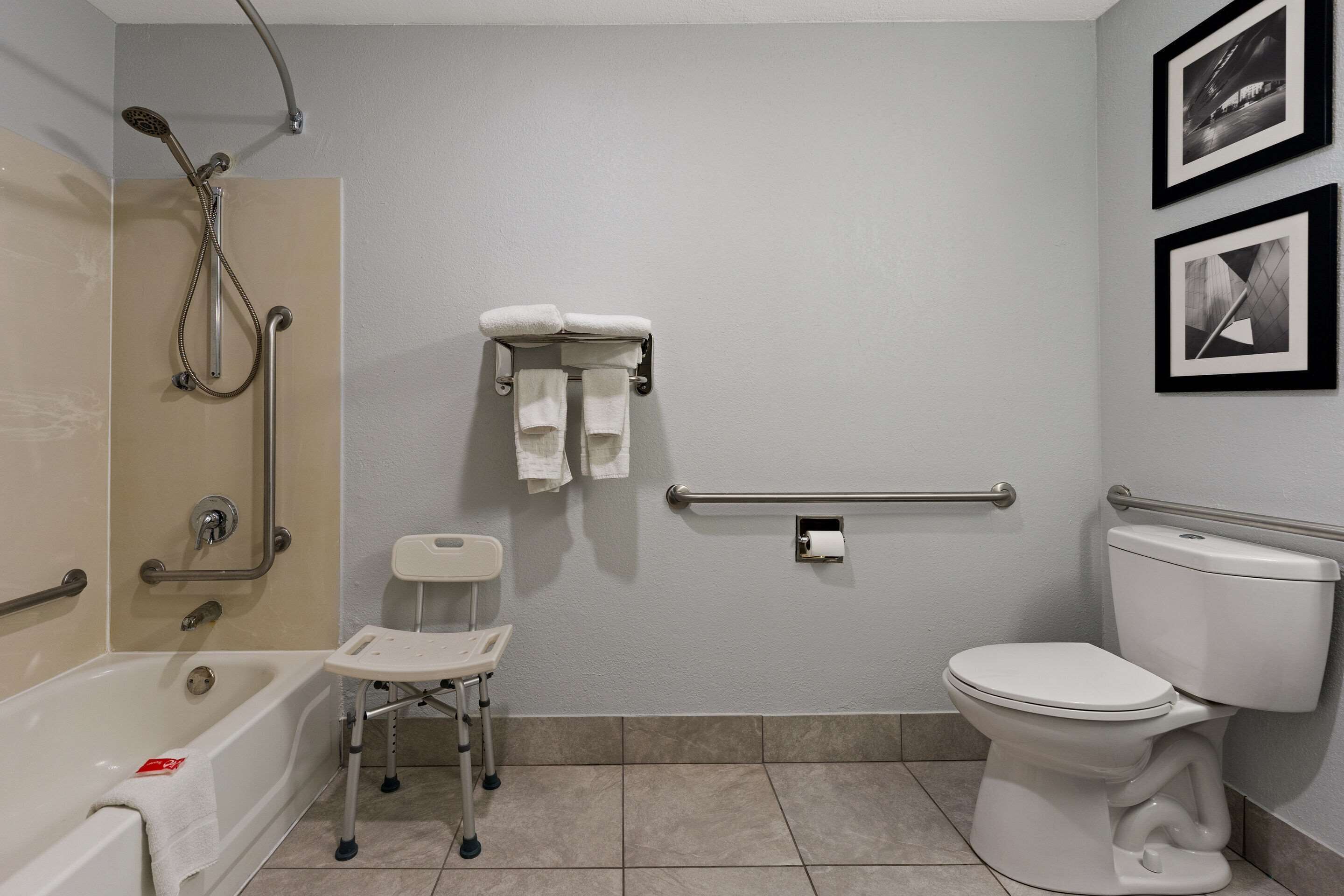 Une salle de bain avec une baignoire, des toilettes et une douche. On y trouve deux serviettes suspendues à un porte-serviettes, un porte-papier toilette et une barre d’appui.