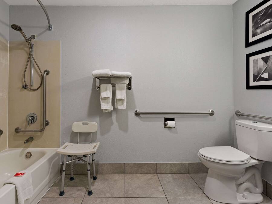 Un baño con bañera, inodoro y ducha. Hay dos toallas colgadas en un perchero, un dispensador de papel higiénico y una barandilla.