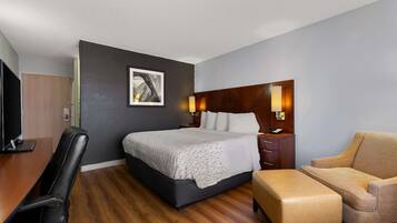 A hotel room with a bed, a desk, a chair, and a bedside table.