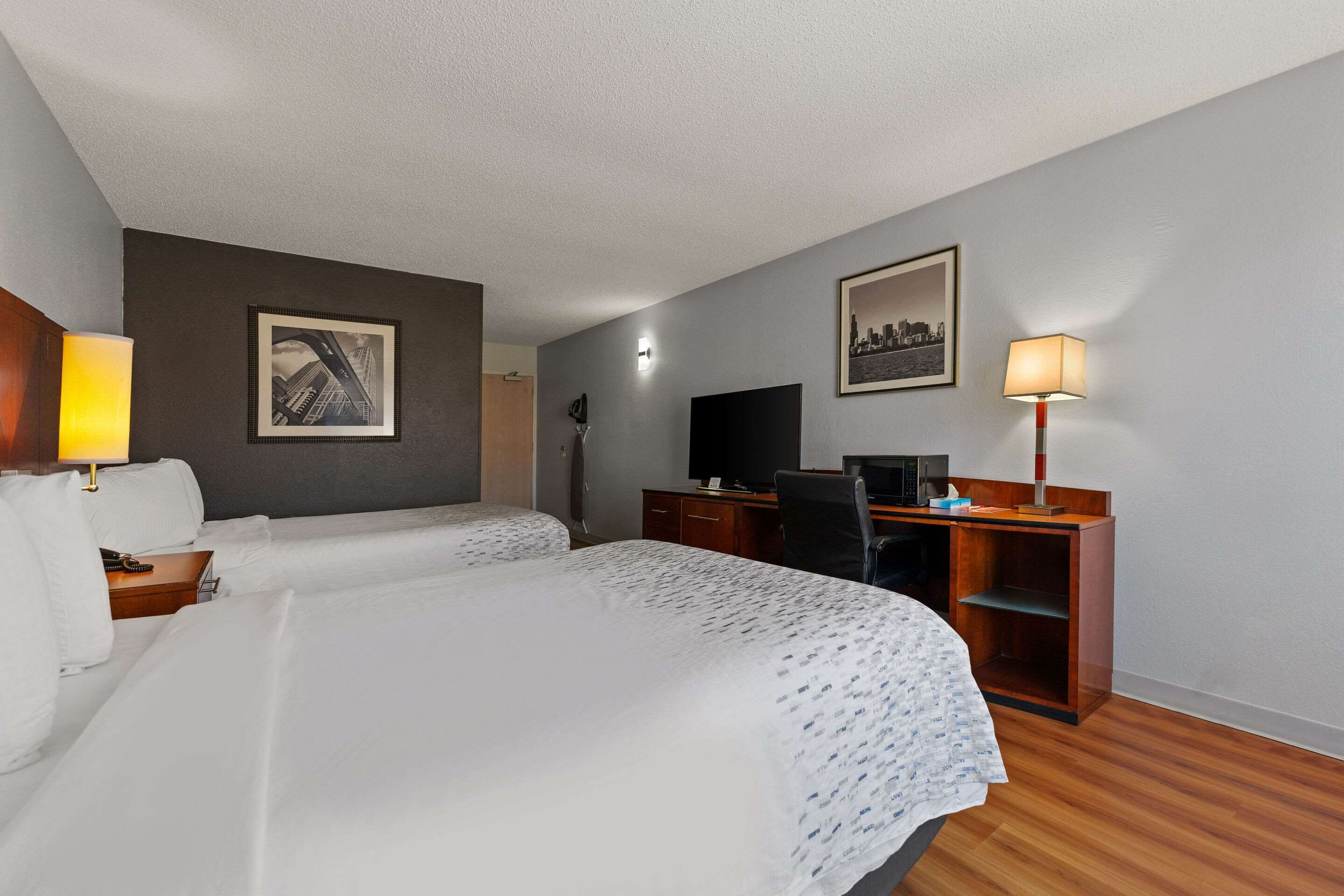 A hotel room with two beds, a desk, a chair, a TV, and a lamp.