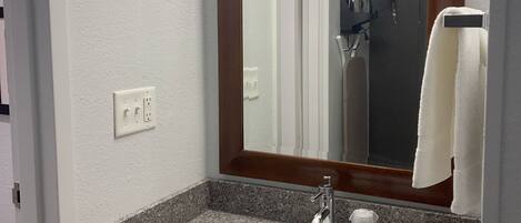 A bathroom with a granite countertop sink, a mirror with a wooden frame, a towel rack, and a towel.