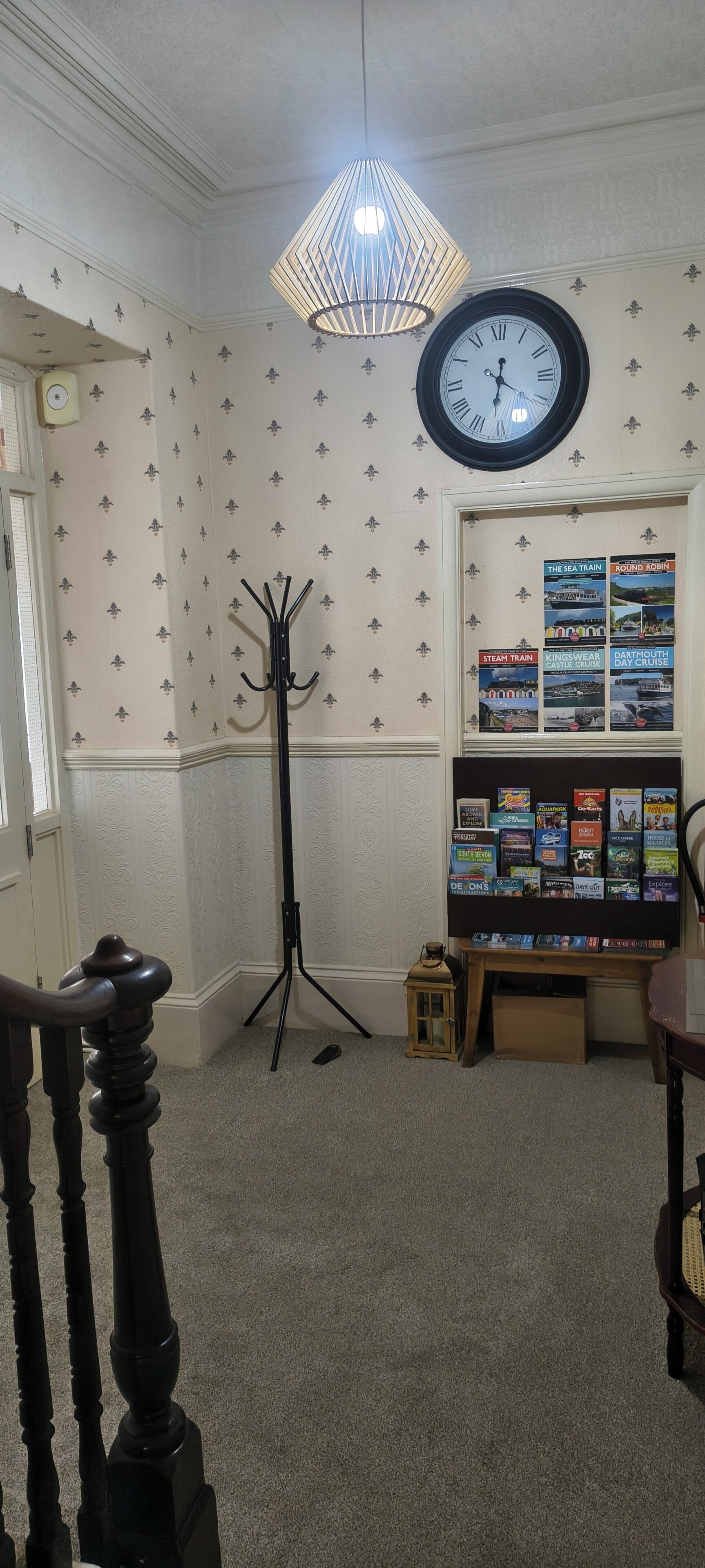 A room with a coat rack, a clock, a lamp, a bookshelf with travel books, and a door.