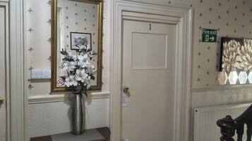A hallway with a white door, a framed picture, a vase with flowers, a 'Fire door keep shut' sign, and a 'Fire exit' sign.